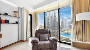 A modern living room with a reclining chair, a bookshelf, and a large window with a cityscape view. - WYZ RENT|3 BDs Address Opera-Burj Khalifa (Dubai)