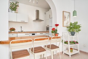 Una cocina moderna con armarios blancos, una isla de madera con taburetes de bar, una campana extractora de acero inoxidable y plantas en macetas.