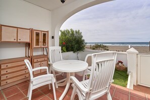 Un patio con una mesa redonda y sillas blancas, un armario de mimbre y vistas a la playa.
