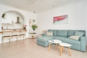 Una sala de estar moderna con un sofá, dos mesas de centro blancas y una cocina con un comedor.