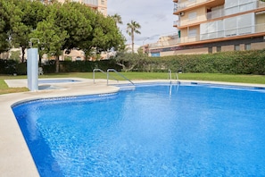 Una piscina con borde de azulejos, rodeada de vegetación y un edificio con un letrero de farmacia.
