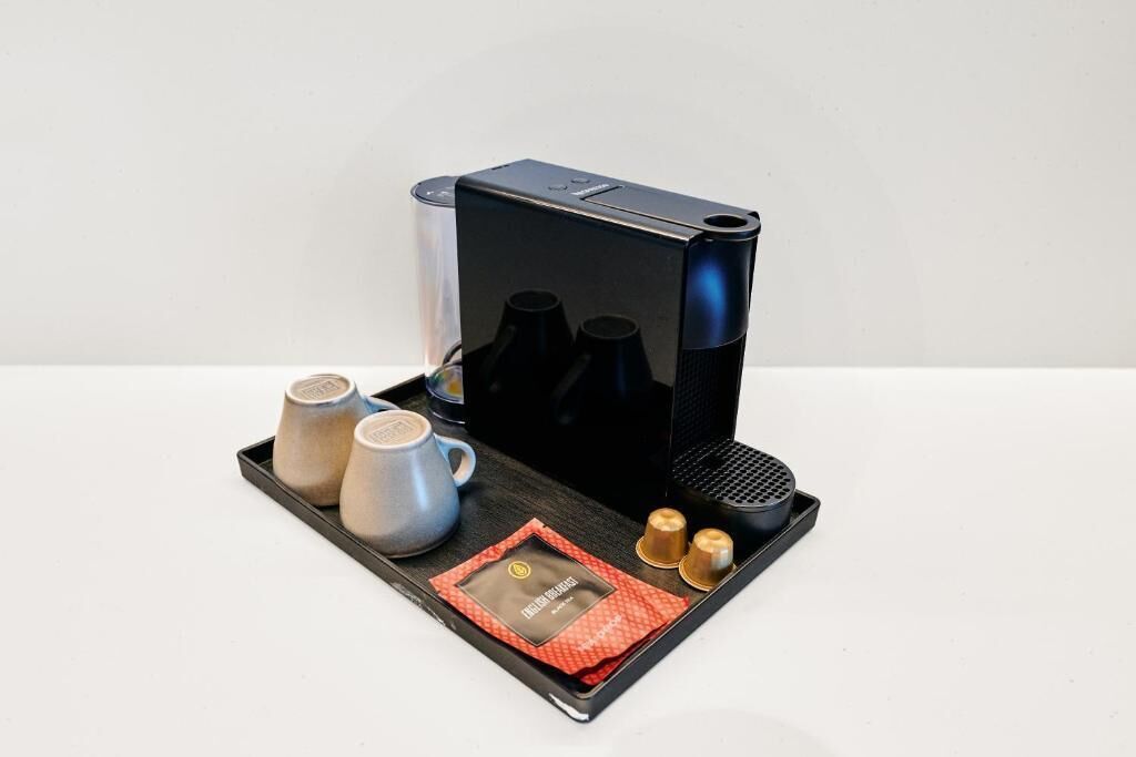 A coffee maker with a tray containing two cups, two small containers, and a packet of coffee pods.