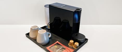 Una cafetera con una bandeja que contiene dos tazas, dos pequeños recipientes y una cápsula de café.