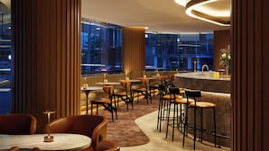 Un restaurante moderno con una zona de bar, mesas redondas y techos altos.