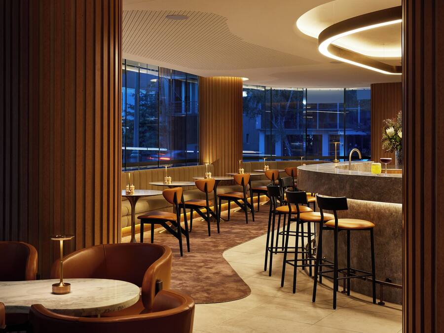 Un restaurante moderno con una zona de bar, mesas redondas y techos altos.