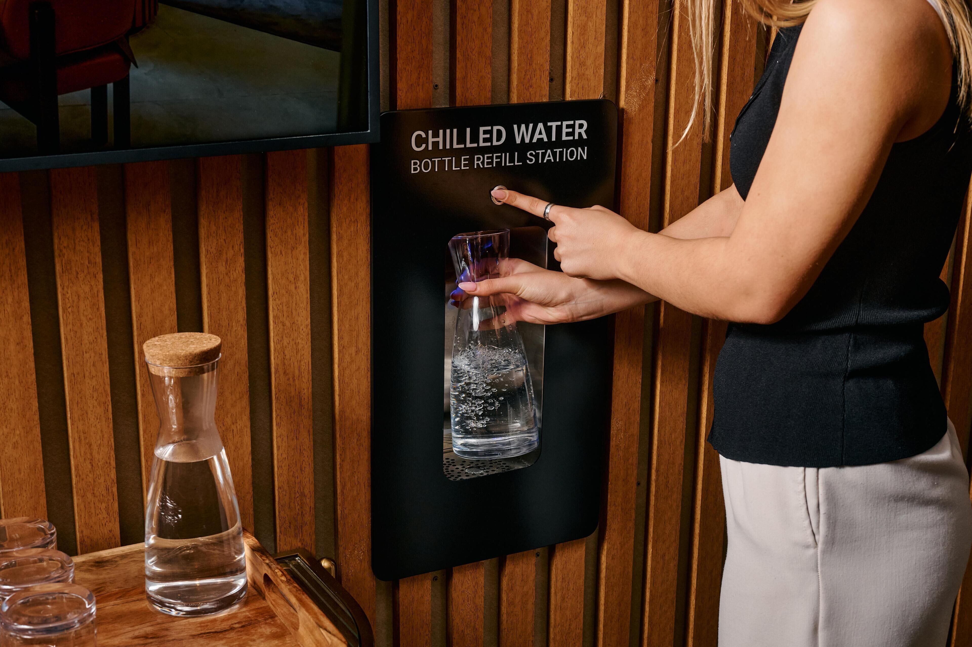 A woman refilling a glass bottle at a chilled water station.