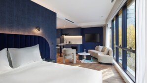 A modern hotel room with a large bed, a seating area with a sofa and chairs, a small table, and a TV mounted on the wall. - Hyatt House South Melbourne (South Melbourne)