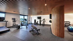 Un gimnasio moderno con varios equipos de ejercicio, un ventanal grande y un diseño de techo de madera.