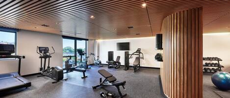 A modern gym with various exercise equipment, a large window, and a wooden ceiling design.