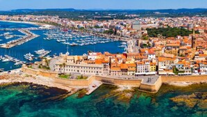 Un paysage urbain côtier avec un port de plaisance, des bâtiments historiques et un rempart fortifié.