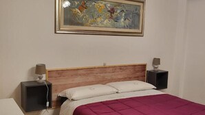 Une chambre à coucher avec une tête de lit en bois, un lit recouvert d’une couverture rose, deux tables de chevet avec des lampes et un tableau abstrait encadré accroché au mur.