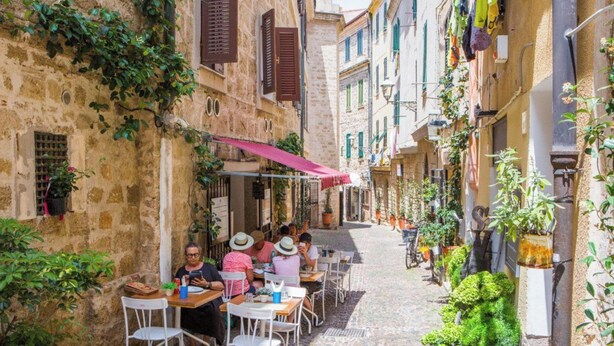 Une rue étroite avec des terrasses, des bâtiments en pierre et des plantes en pot.