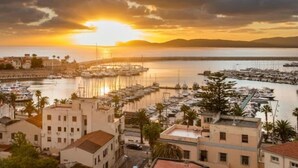 Une ville côtière dotée de bâtiments historiques, d’un port de plaisance avec des bateaux et offrant un magnifique coucher de soleil sur l’eau.