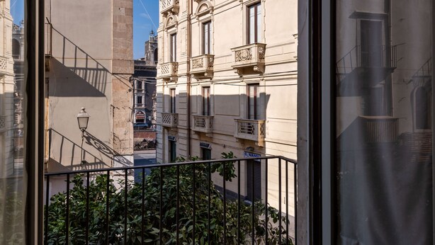 A narrow street with buildings on either side, a metal railing in the foreground, and a clear sky. - Casa all Anfiteatro di Catania by Wonderful Italy (Catania)