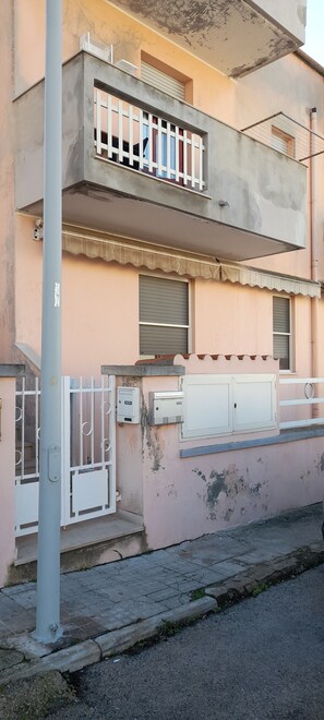 A two-story building with a balcony, a gated entrance, and a utility box.
