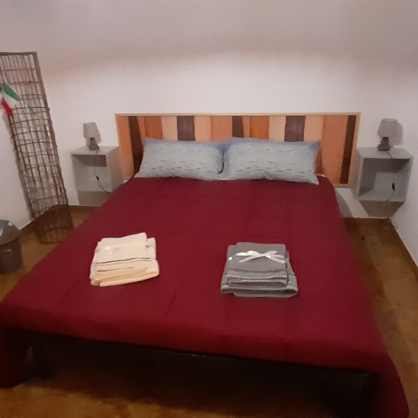 A bed with a red bedspread, two pillows, and folded towels on the bed.