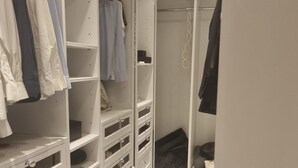 Tilava vaatehuone, jossa on useita hyllyjä ja laatikoita, vaatetanko sekä suihkutila, jossa on suihkuverho.