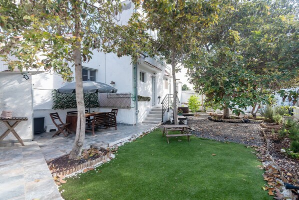 A patio with a table and chairs, a small lawn, and a white building with a covered seating area.