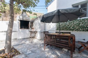 A patio with a wooden table, a grill, and an umbrella.