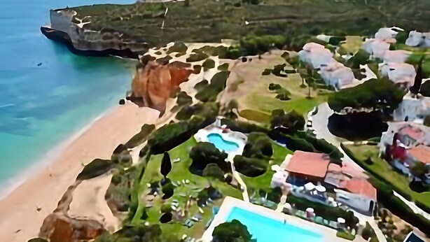Luchtbeeld van een kustbezit met een strand, zwembad en weelderige begroeiing.