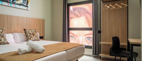 Habitación de hotel con cama, escritorio, silla y vista a un paisaje urbano a través de un ventanal grande.
