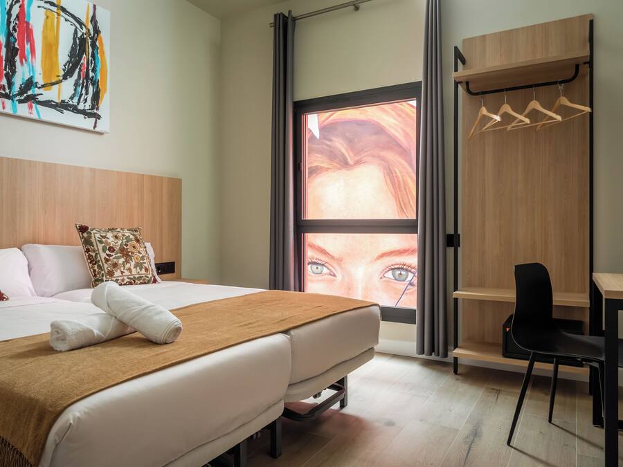 Une chambre d’hôtel équipée d’un lit, d’un bureau, d’une chaise et offrant une vue sur le paysage urbain grâce à une grande fenêtre.