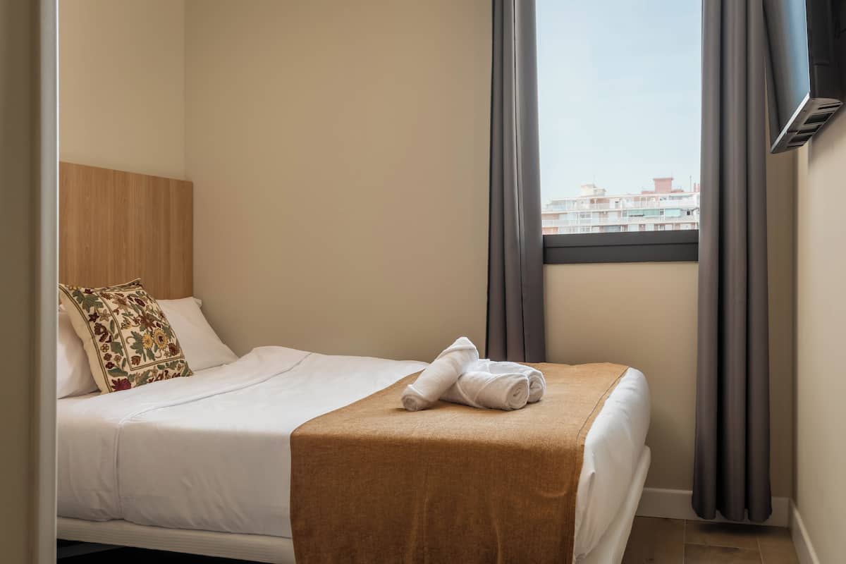 A neatly made bed with a white duvet, a brown throw blanket, and a floral pillow.