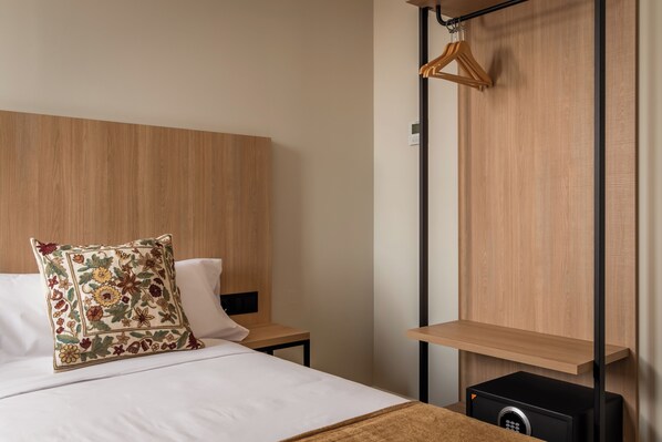 A hotel room with a wooden headboard, a bed with white linens, a floral pillow, a bedside table, and a black safe.