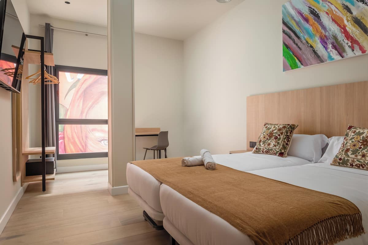 A modern hotel room with a large bed, a desk, and a colorful abstract painting on the wall.