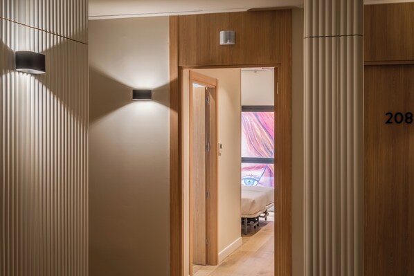 Un pasillo de hotel con una puerta de madera que da a una habitación con una cama y una obra de arte colorida en la pared.