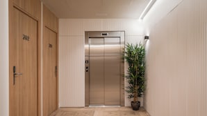 Un pasillo con puertas de madera numeradas 201 y 202, un ascensor y una planta en maceta.