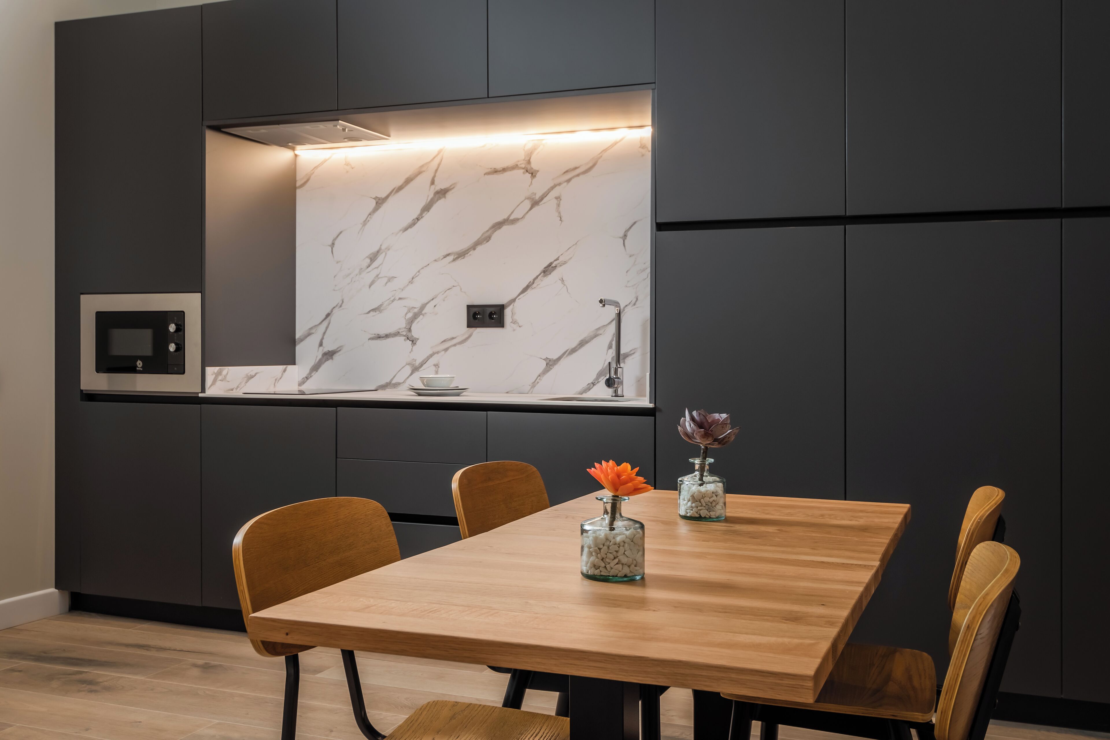 A modern dining area with a marble backsplash, a built-in oven, and a wooden dining table with chairs.