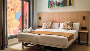 Una cama doble con dos almohadas, cabecera de madera, mesita de noche y ventana con cortinas.