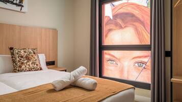 Una habitación de hotel con cama, ventana con vistas, cabecera de madera y almohada floral.