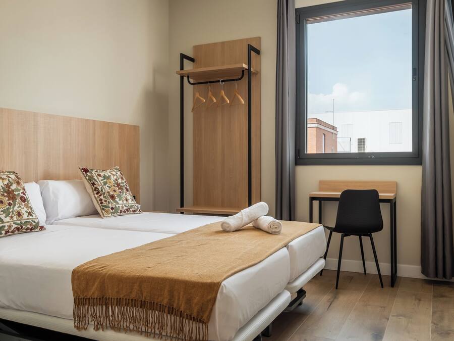 Habitación de hotel con cama, escritorio y ventana con cortinas.