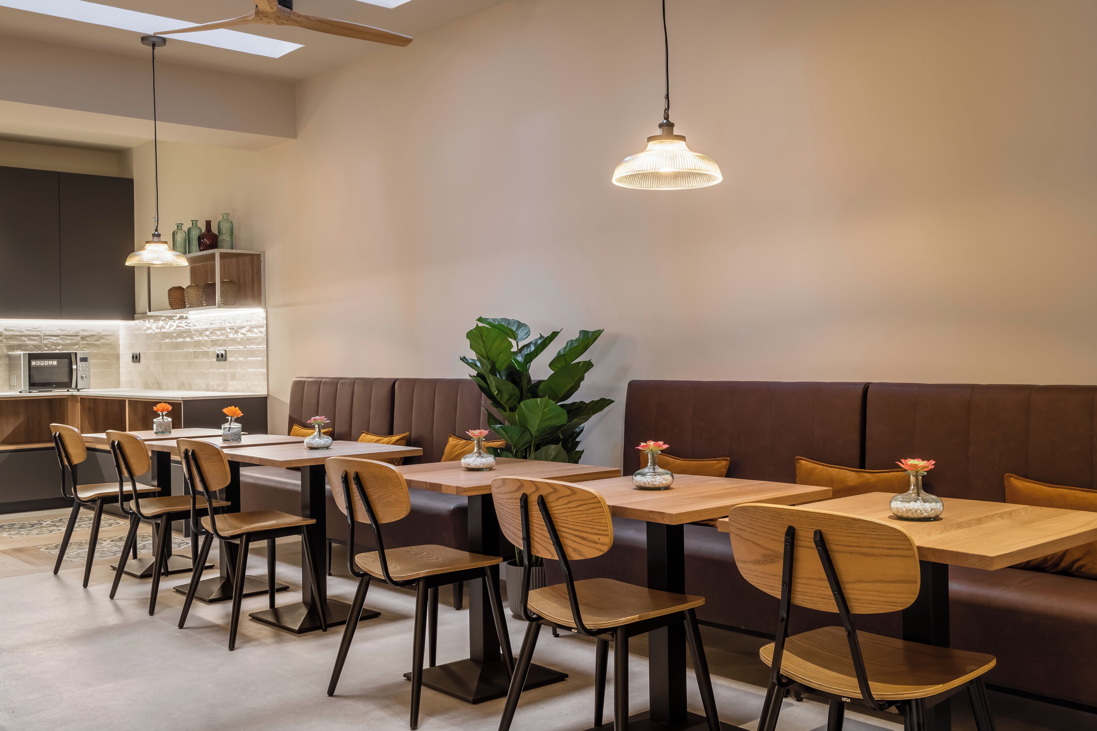 A modern dining area with wooden tables and chairs, a brown cushioned bench, and pendant lighting.