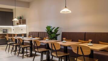 A modern dining area with wooden tables and chairs, a brown cushioned bench, and pendant lighting.