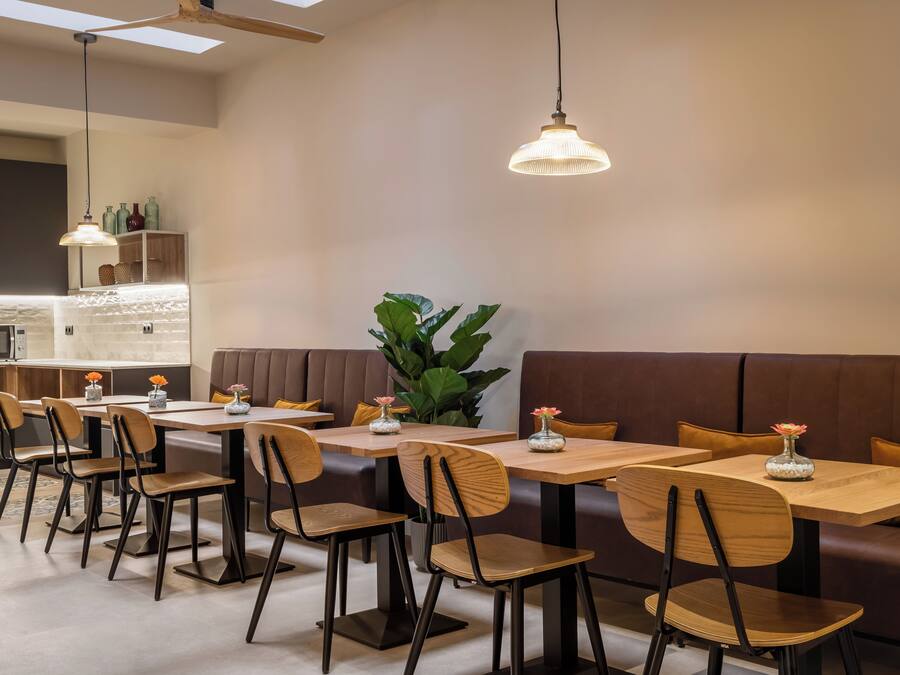 A modern dining area with wooden tables and chairs, a brown cushioned bench, and pendant lighting.