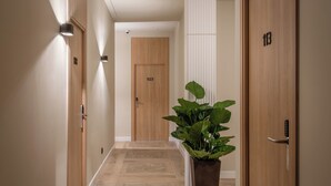 Un pasillo con puertas de madera numeradas 103 y 113, una planta en maceta y una lámpara en la pared.