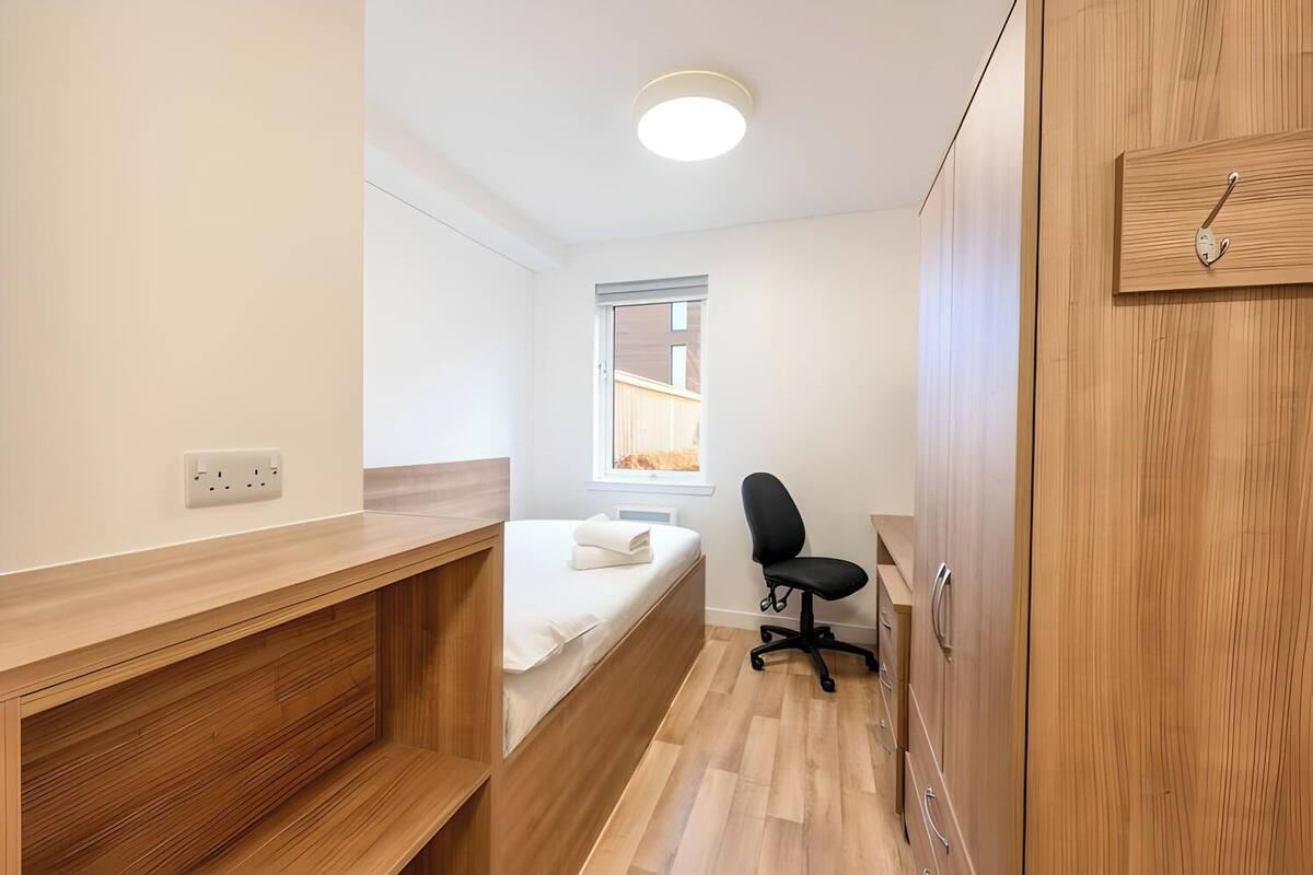 Ein kleines Zimmer mit Bett, Schreibtisch und Kleiderschrank.