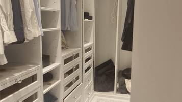 A walk-in closet with multiple shelves and drawers, a hanging rod, and a shower area with a curtain.