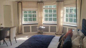 A bedroom with a bed, a desk, and two windows with curtains. - Park Village East Apartment - London (London)