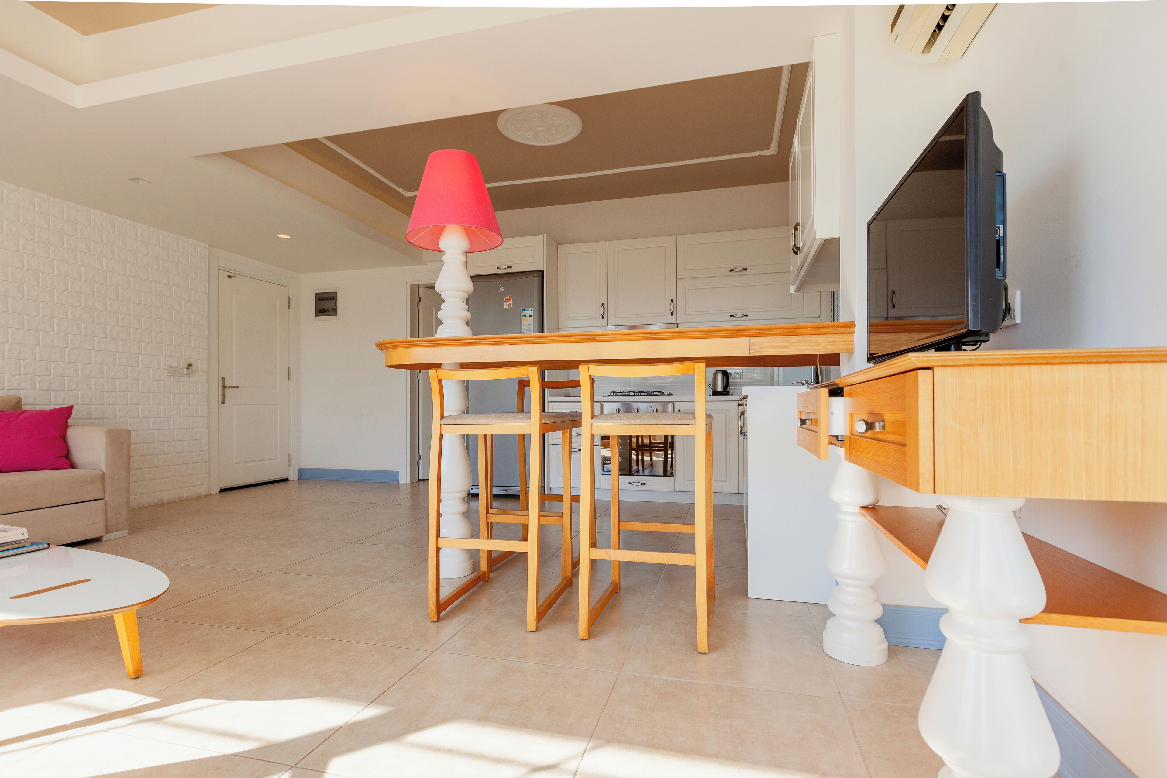 Una cocina moderna con armarios blancos, una mesa de comedor de madera y una lámpara roja.