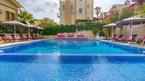 A swimming pool with lounge chairs and umbrellas, surrounded by buildings and greenery. - Kalkan Suites Hotel (Kas)