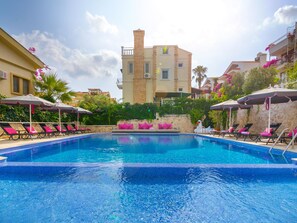 A swimming pool with lounge chairs and umbrellas, surrounded by buildings and greenery. - Kalkan Suites Hotel (Kas)