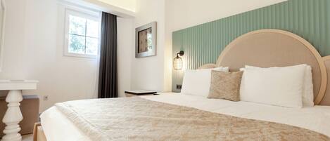 A hotel room with a large bed, a bedside table, a nightstand, a window with curtains, and a wall-mounted lamp.