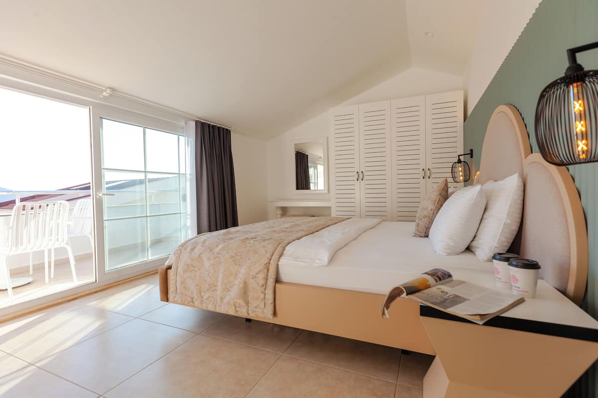 A bedroom with a bed, a bedside table with a lamp, a window, and a view of the outside.