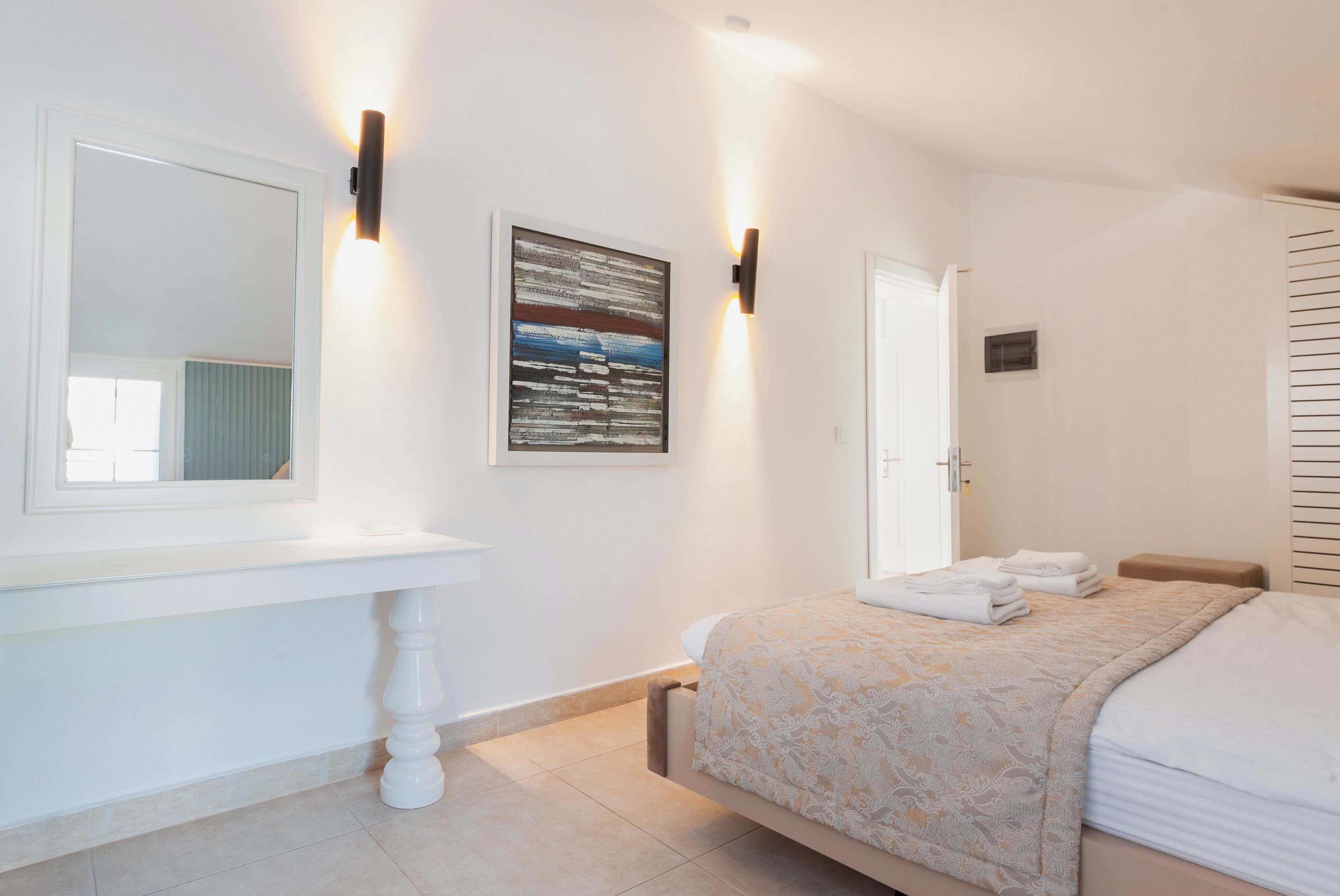 A bedroom with a bed, a bedside table, a mirror, and a wall-mounted light fixture.