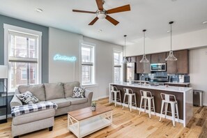 Un salon moderne avec un canapé, une table basse et des tabourets de bar. Un panneau néon affiche le mot « Cincinnati ».