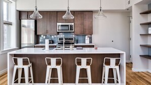 Een moderne keuken met donkere houten kastjes, roestvrijstalen apparatuur, een wit kookeiland met barkrukken en hanglampen.